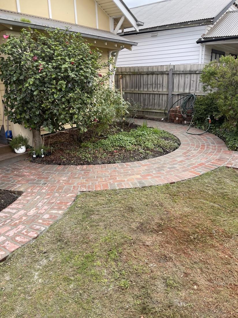 Reclaimed brick garden path curving around a garden bed