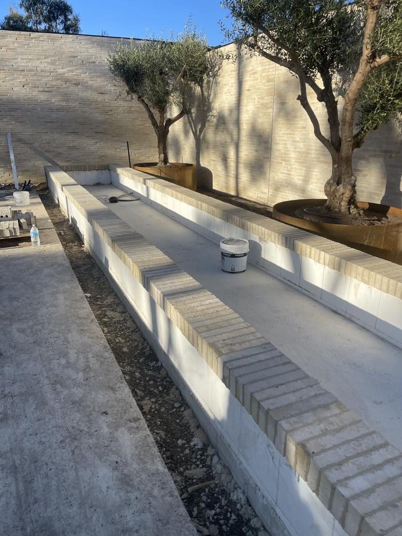 Garden bed walls finished with a light brick header capping beside olive trees in corten planters