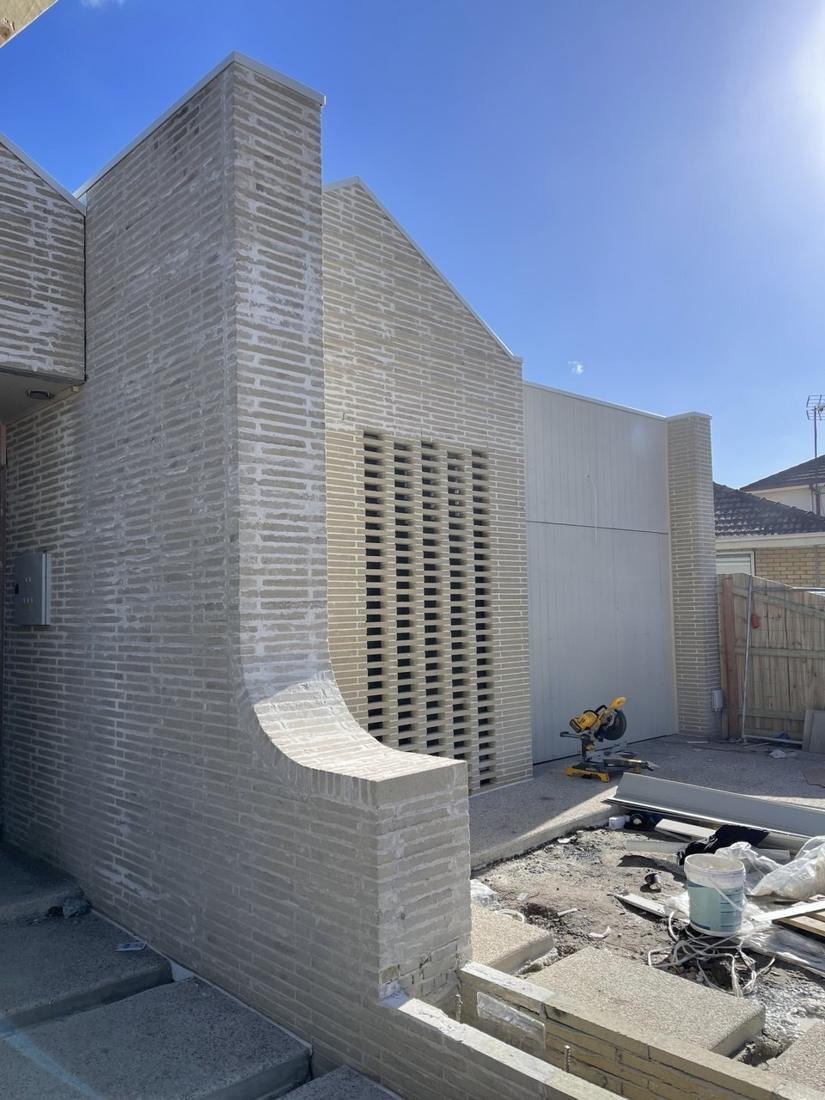 Long-format light brick facade with a curved wing wall and a vertical slotted brick screen